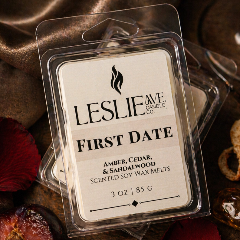 Scented wax melts packaging labeled 'First Date' by Leslie Ave on a decorative surface with red petals and a glass.
